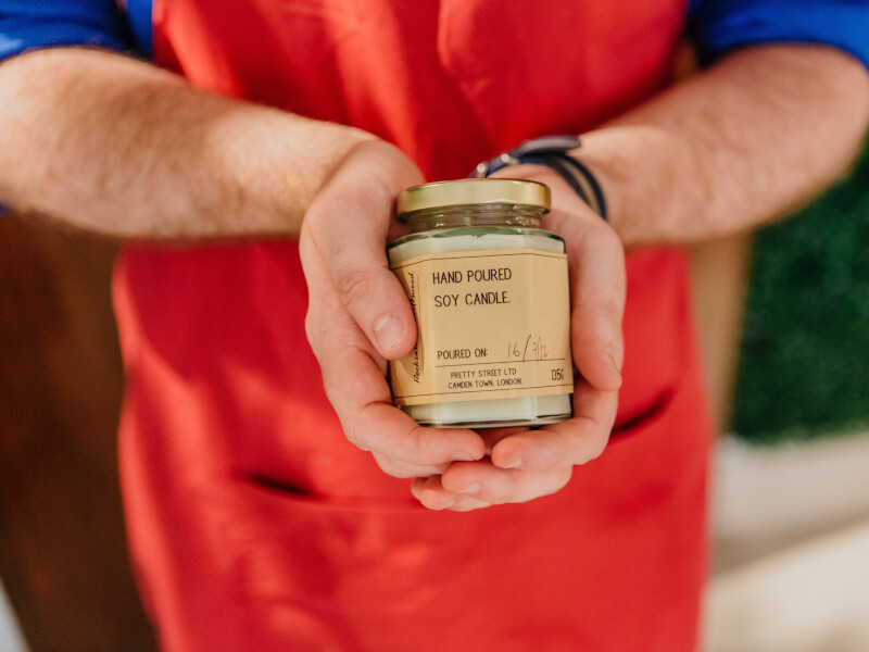 Hands holding a hand poured soy candle in a glass hexagonal jar with gold lid